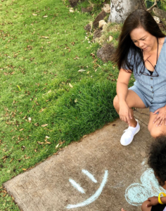 Daneen Sandry with child drawing chalk on concrete near grass