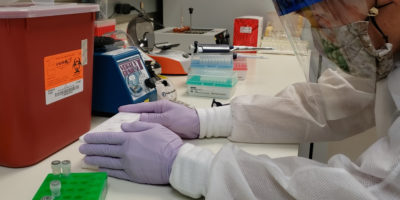 DOH lab technician handling a tray of vials
