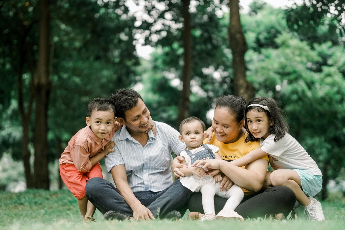 a 5-person family with small children gathered in a green park