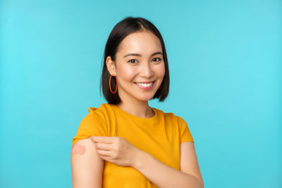 woman smiling and lifting shirt sleeve to show Band-Aid on arm.